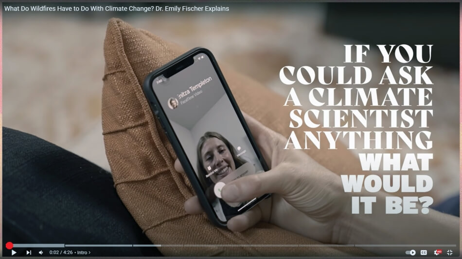 A screenshot from an ad produced by The Science Moms. Text is superimposed over a close-up of a pale hand holding a smart phone that shows a virtual phone call. The text reads: “If you could ask a climate scientist anything, what would it be?”