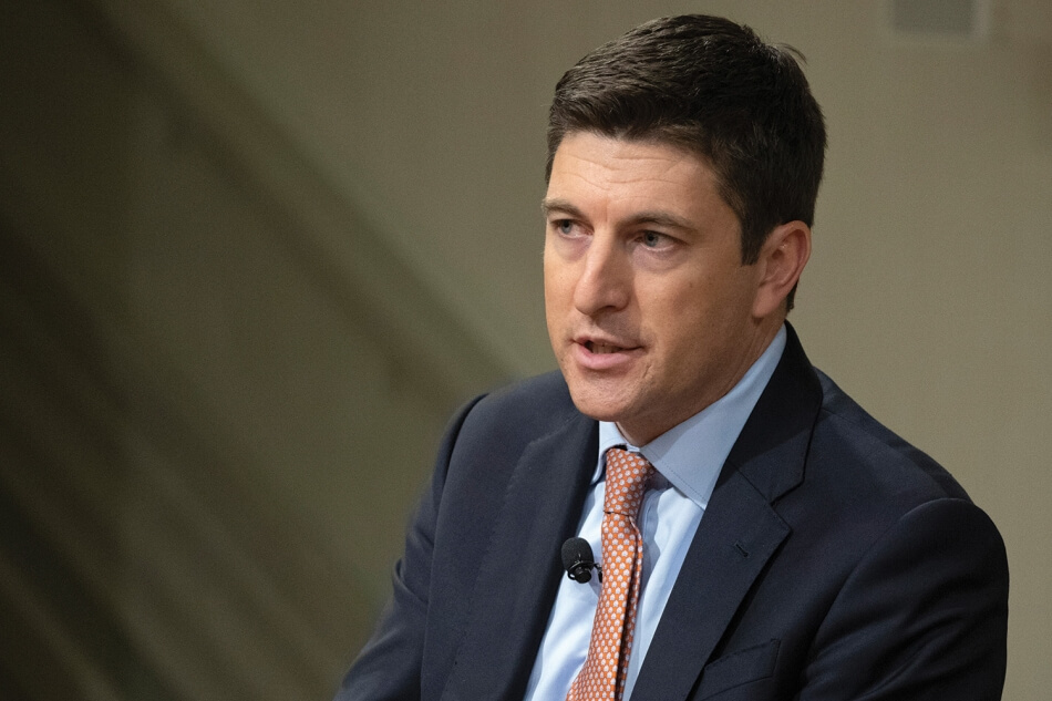 A photo of Representative Bryan Steil, a man with pale skin and short dark hair. He wears an orange tie, a pale blue shirt, and a dark blue suit. A microphone is clipped to his tie. Photo by Martha Stewart Photography.