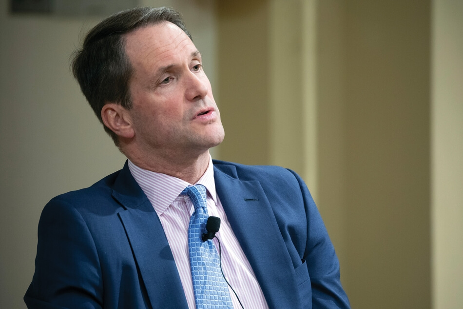 A photo of Representative Jim Himes, a man with pale skin and short dark hair. He wears a blue tie, a pale purple shirt, and a dark blue suit. A microphone is clipped to his tie. Photo by Martha Stewart Photography.