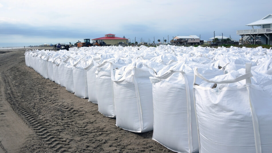 A wall of sandbags line the coast in Grand Isle, Louisiana. The bags are in the foreground with the town huddled behind them.