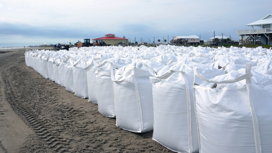 Photo by Team New Orleans, U.S. Army Corps of Engineers. Published under a Creative Commons Public Domain Mark 1.0 license. A wall of sandbags line the coast in Grand Isle, Louisiana. The bags are in the foreground with the town huddled behind them.