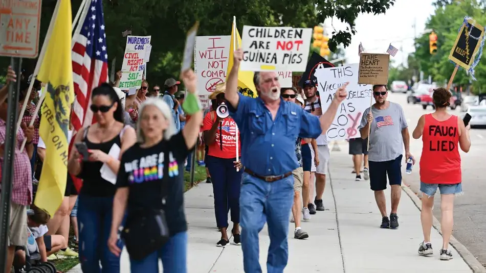 Photo by Anthony Crider. Published under a Creative Commons Attribution-NonCommercial 2.0 Generic (CC BY-NC 2.0) license. An interior image from the fall 2023 issue of Dædalus. Protestors at a “freedom of choice” rally in September 2021 pace on a sidewalk and some walk in the streets holding handwritten signs or wearing shirts with text on them, some of which read: “Children are not guinea pigs,” “Fauci lied,” and “I will not comply.” Photo by Anthony Crider. Published under a Creative Commons Attribution-NonCommercial 2.0 Generic (CC BY-NC 2.0) license.