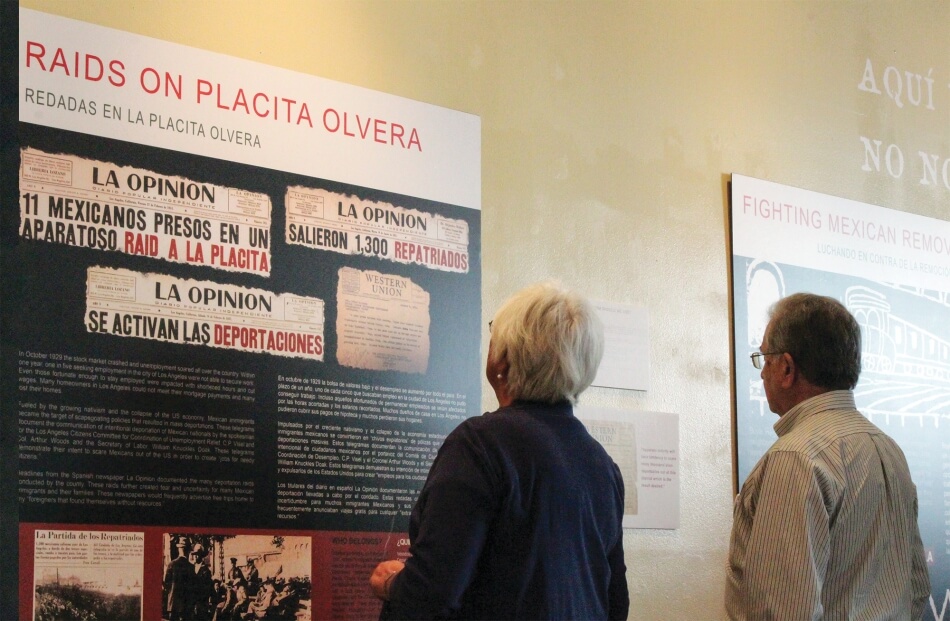 Courtesy of Michelle Vasquez-Ruiz Two visitors examine the Boyle Heights Museum exhibition Aquí Estamos Y No Nos Vamos at CASA 0101 in East Los Angeles, 2017