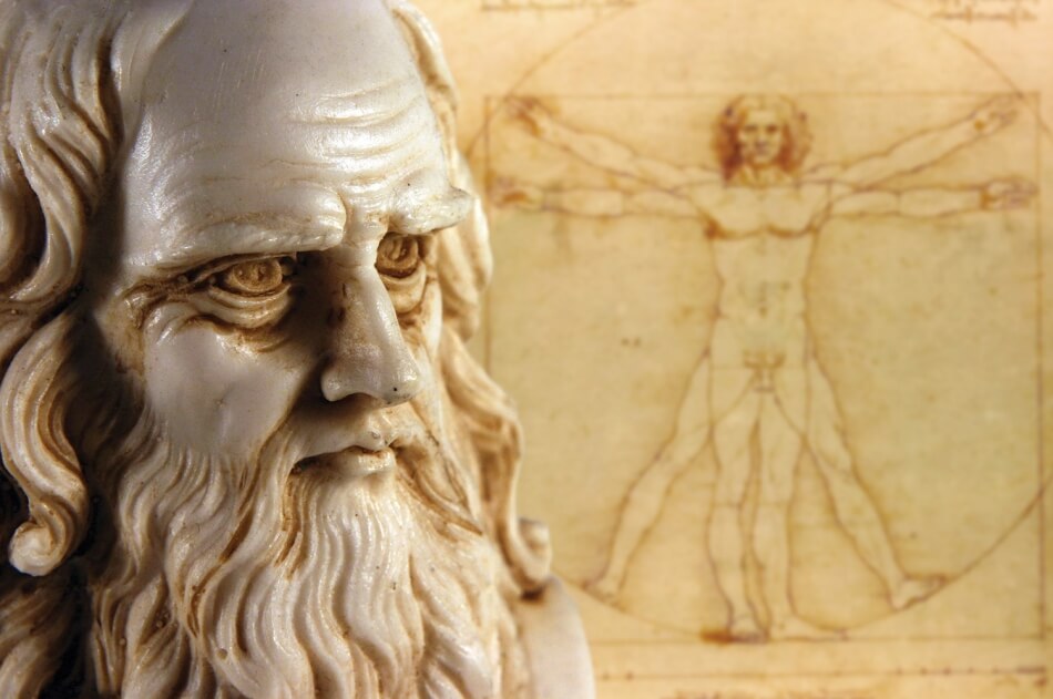 Photo by iStock.com/Myper. The head of a sculpture of Leonardo da Vinci with a full beard is in focus in the foreground beside da Vinci’s drawing The Vesuvius Man, which is out of focus in the background. Photo by iStock.com/Myper.