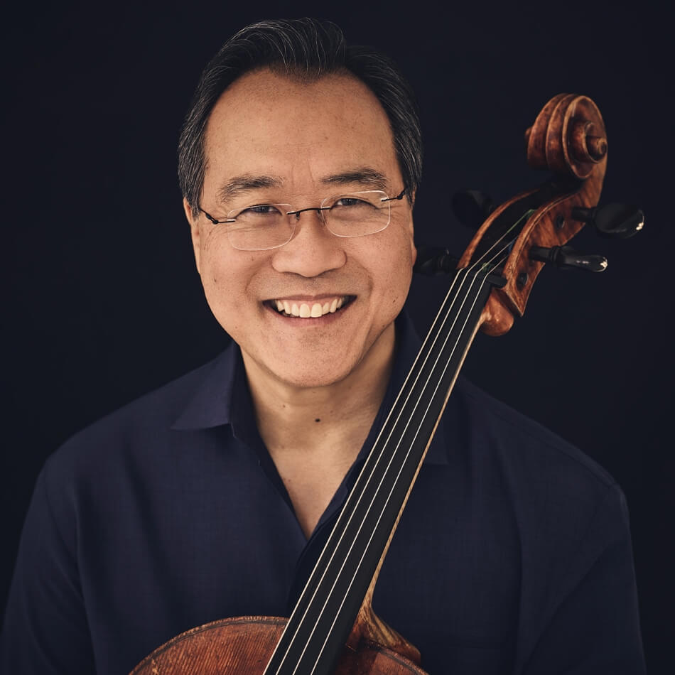 A headshot of Yo-Yo Ma. He has brown skin and short gray hair, and wears a dark blue collared shirt. He holds a cello in his lap. Photo by Jason Bell.