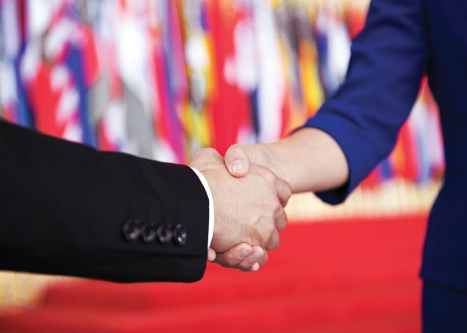 iStock.com/baona Handshake with many different country flags in the background, United Nations