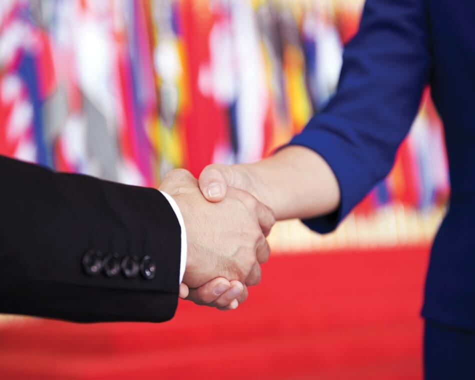 Man and woman shaking hands at UN with flags behind them. iStock.com/baona