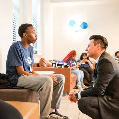 A man in a business suit bends down to talk to a seated male high school student