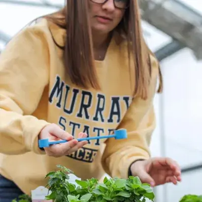A young woman wearing a sweatshirt working on potted plants in a greenhouse
