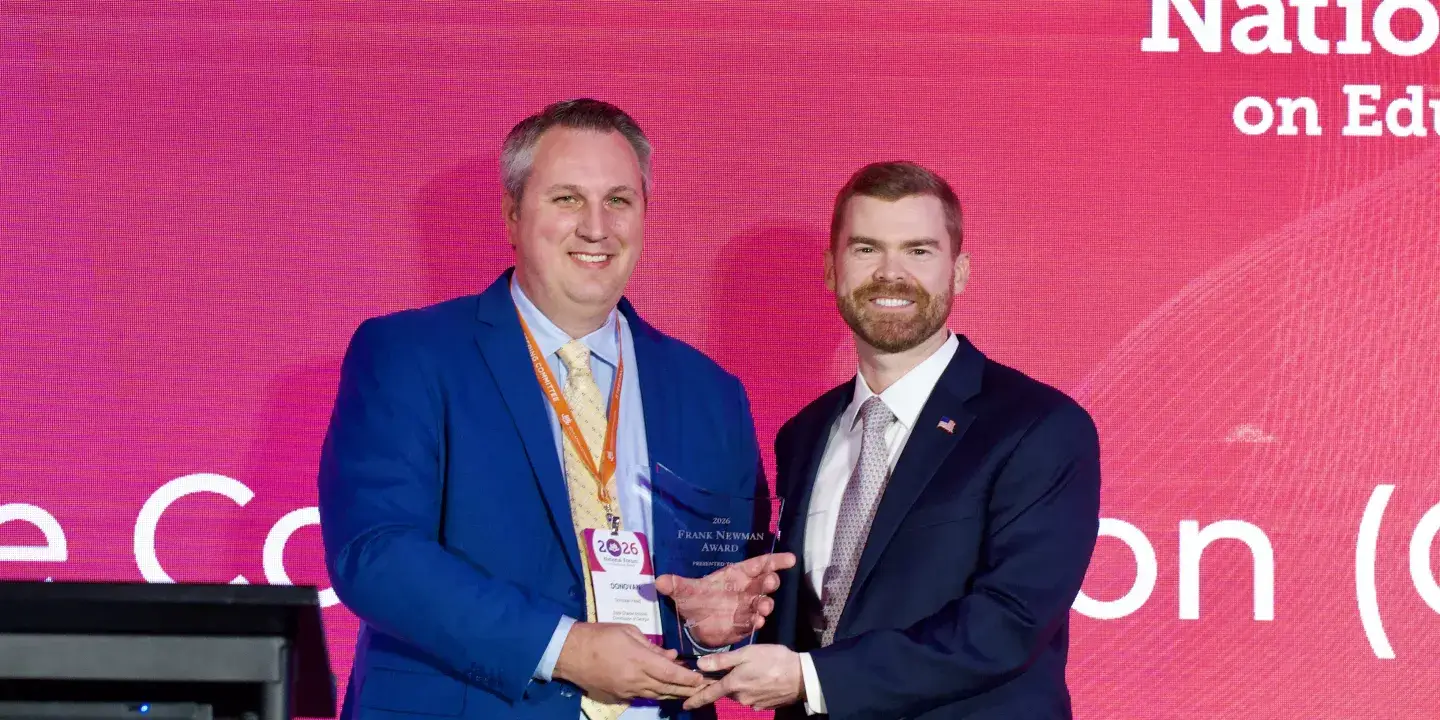 Two men in business attire smile toward the camera and hold a glass award.