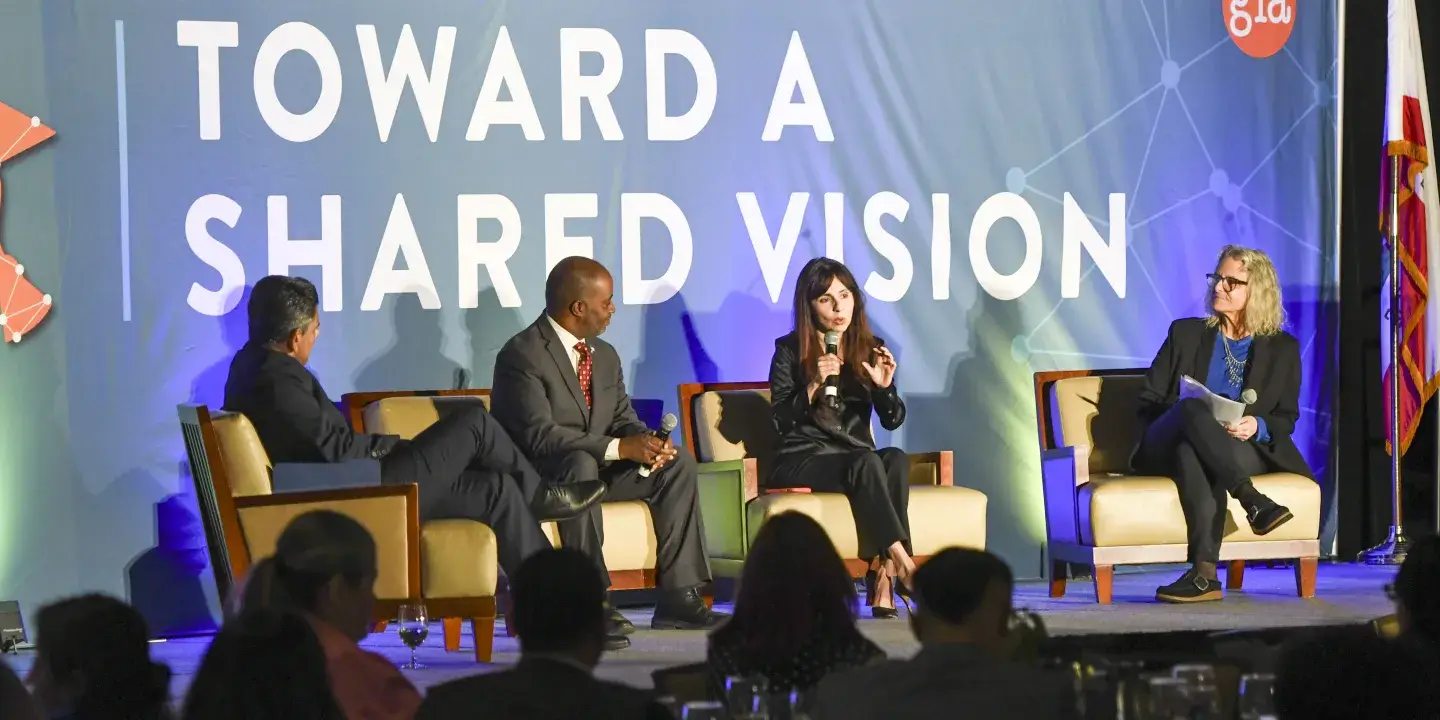 Panelists on stage at a conference with a sign behind them that reads "toward a shared vision"