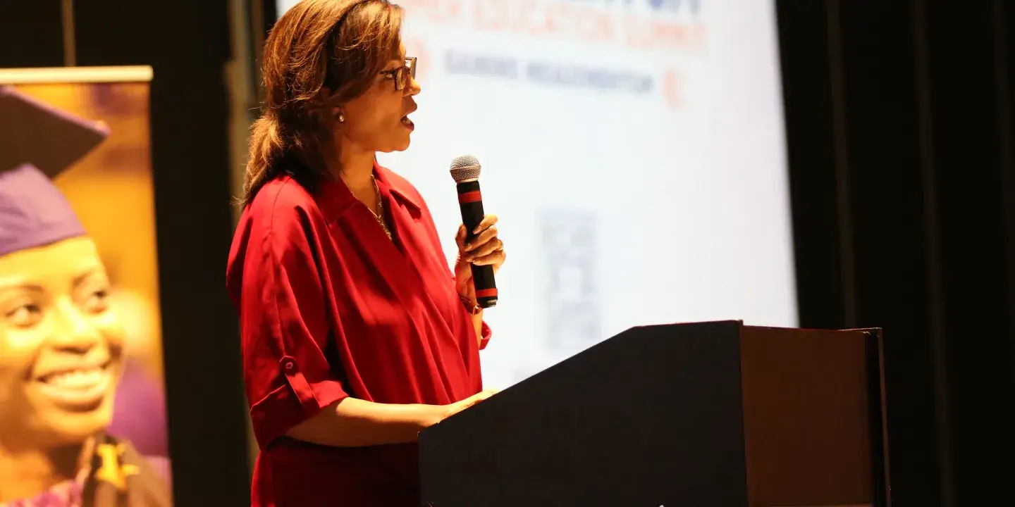 A woman stands in front of a powerpoint back drop during a presentation
