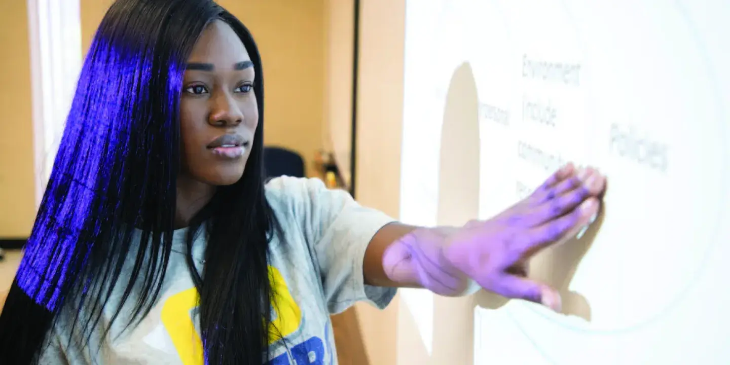 A young Black woman pointing at something on a powerpoint screen
