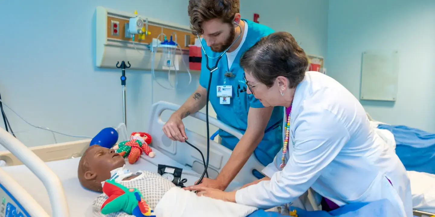 Two young men in health uniforms practicing a medical procedure on a dummy