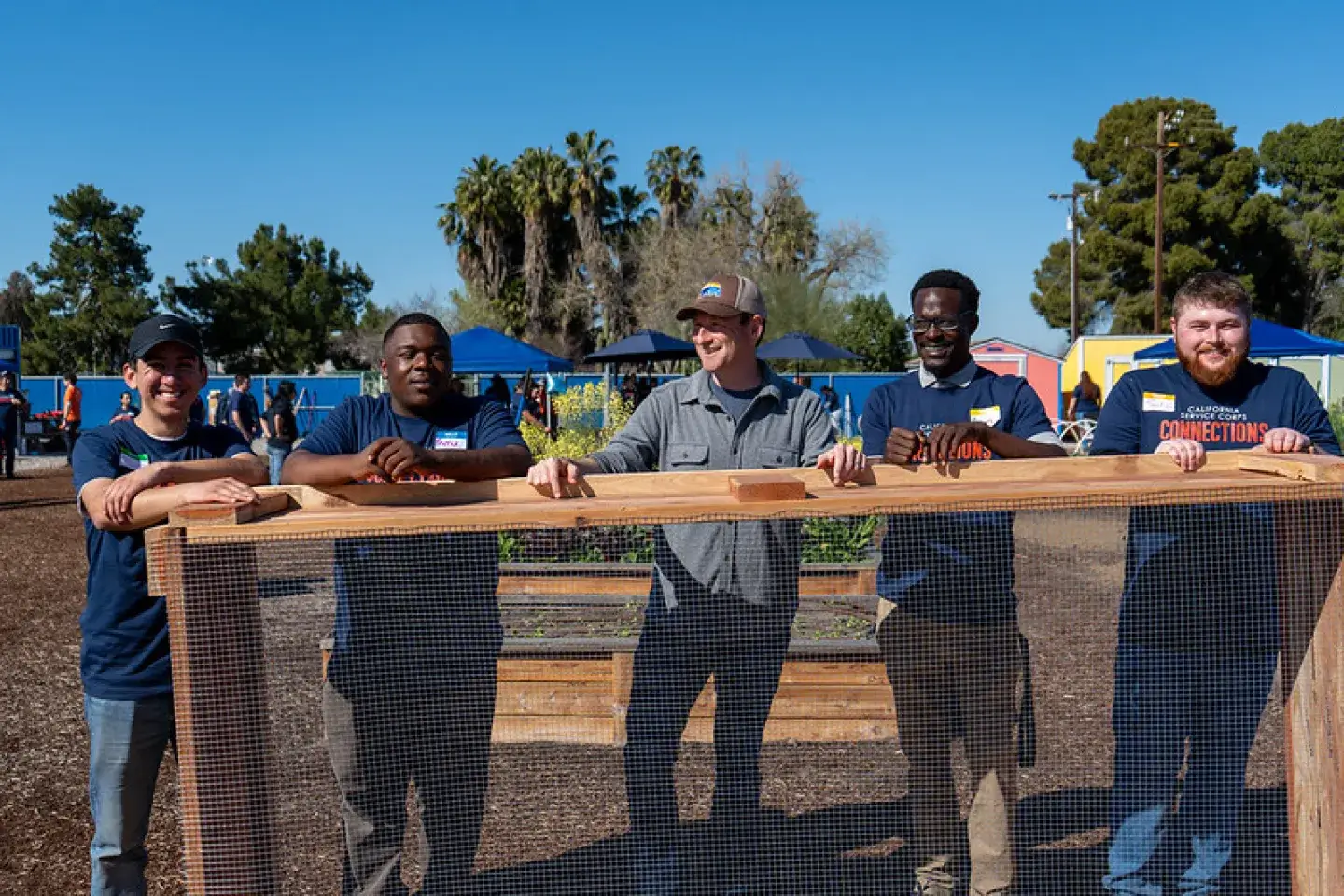 5 men stand in front of a tall wooden table with matching shirts 