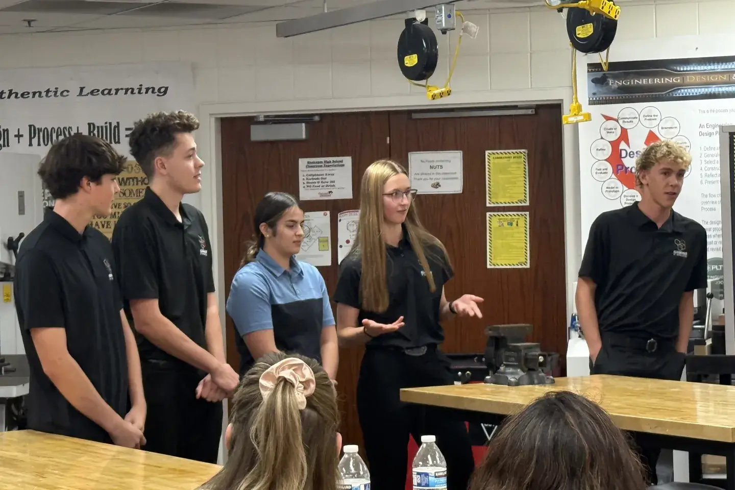 Students stand at front of classroom.