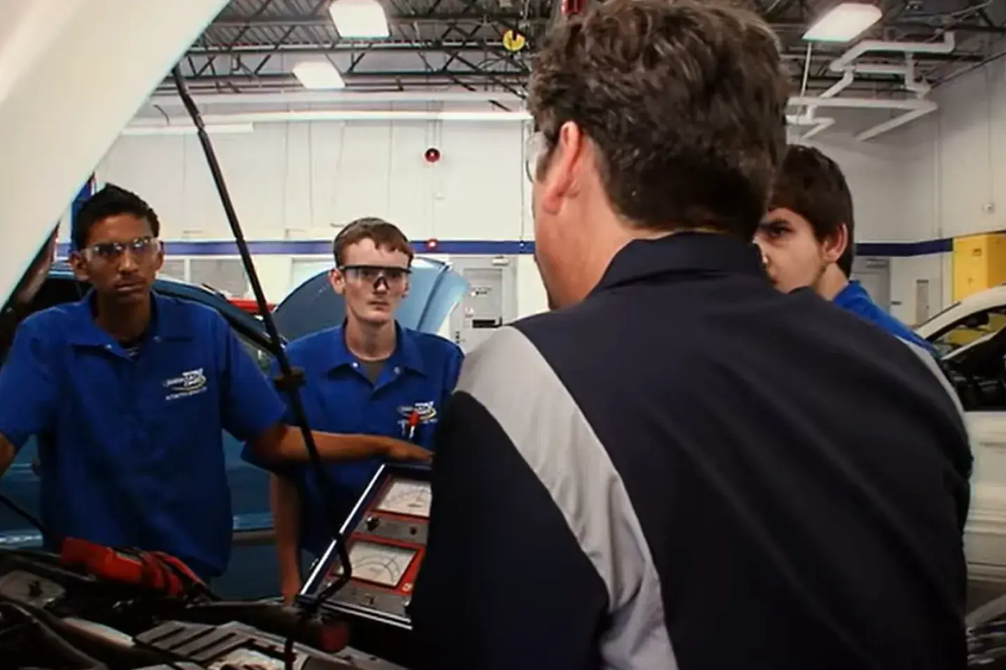 A few male students working on a car while an older male teaches them