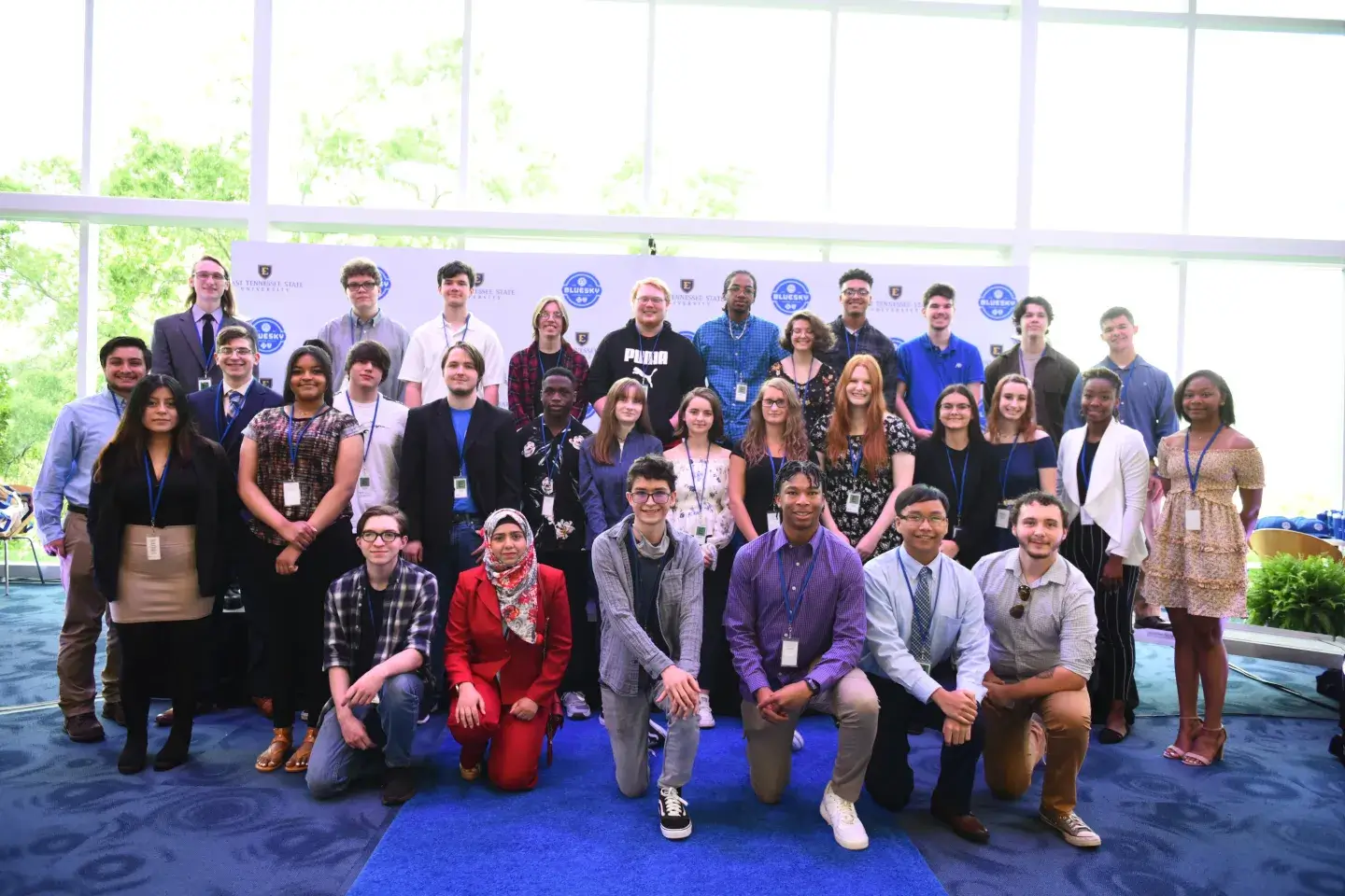 A large group of diverse students posing for a photo with a blue carpet and background
