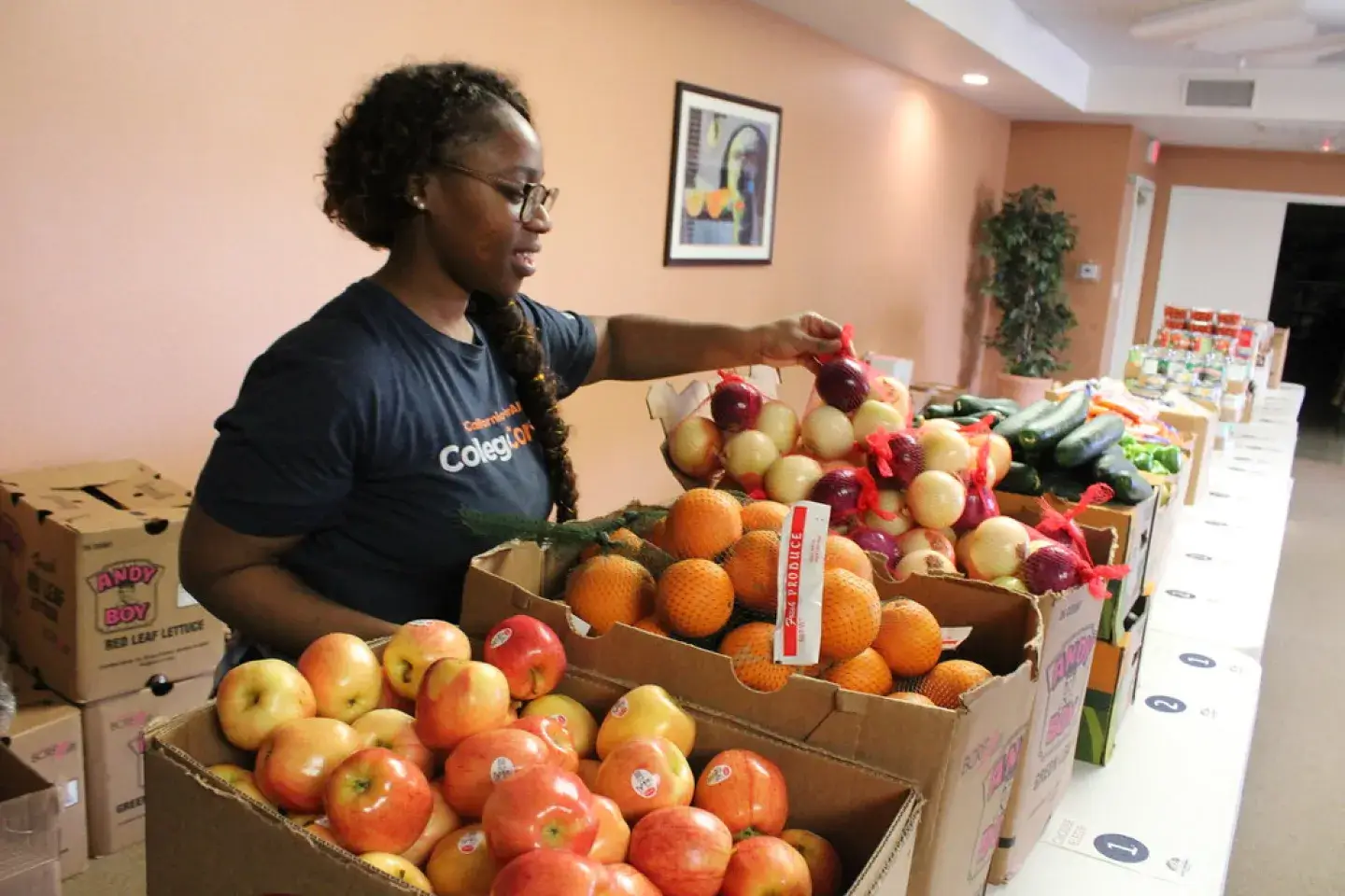 A Black woman places fruit into boxes at a long table in a food pantry.