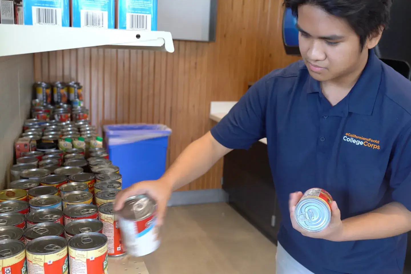 A college volunteer places a can on a shelf at a food pantry.