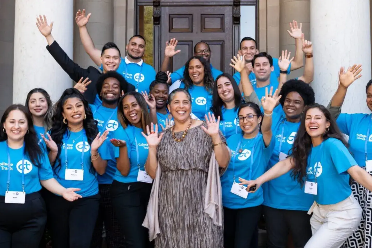 A group of students posing for a photo with their arms wide, all in matching blue t-shirts