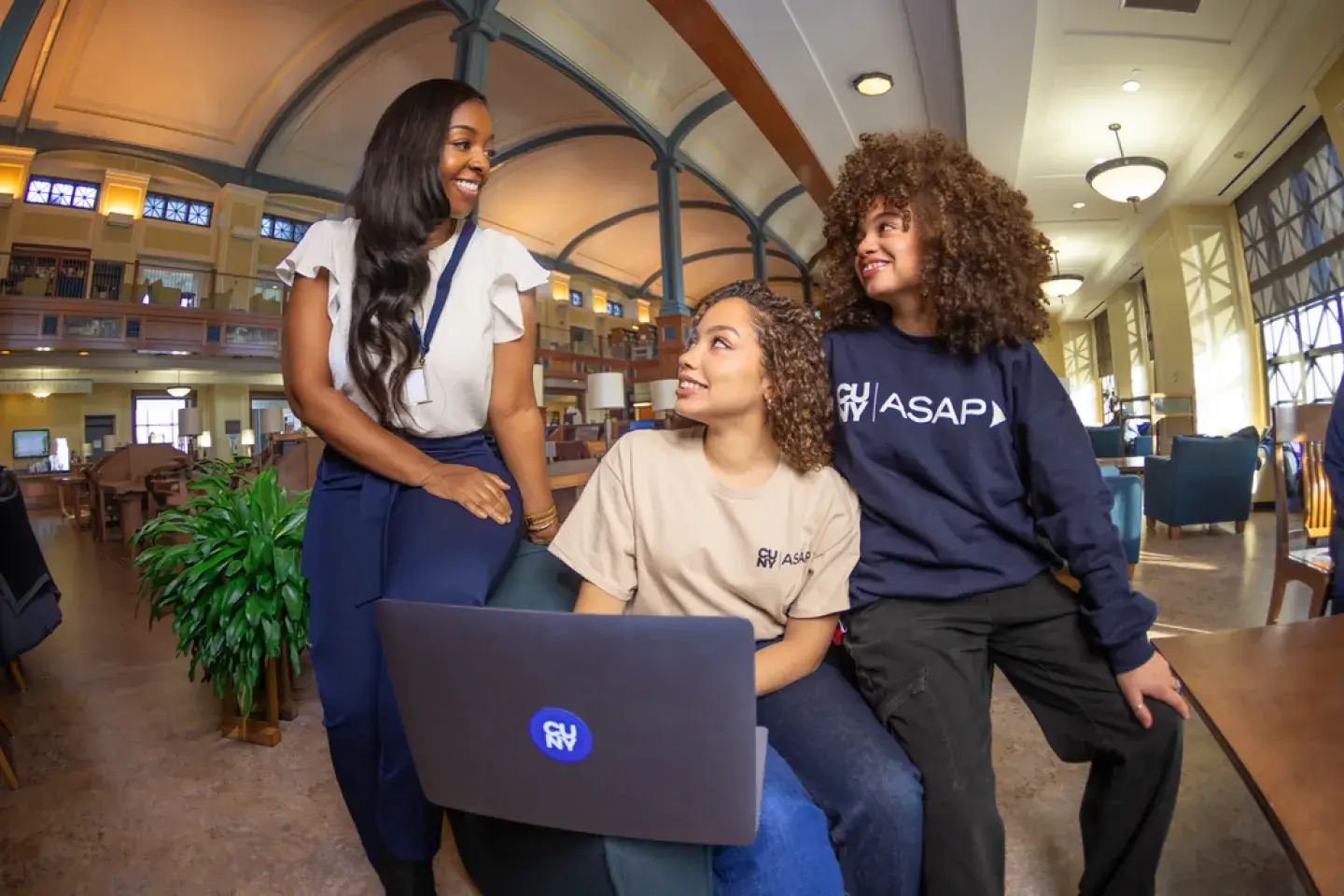 Three female college students seated around a computer, smiling 