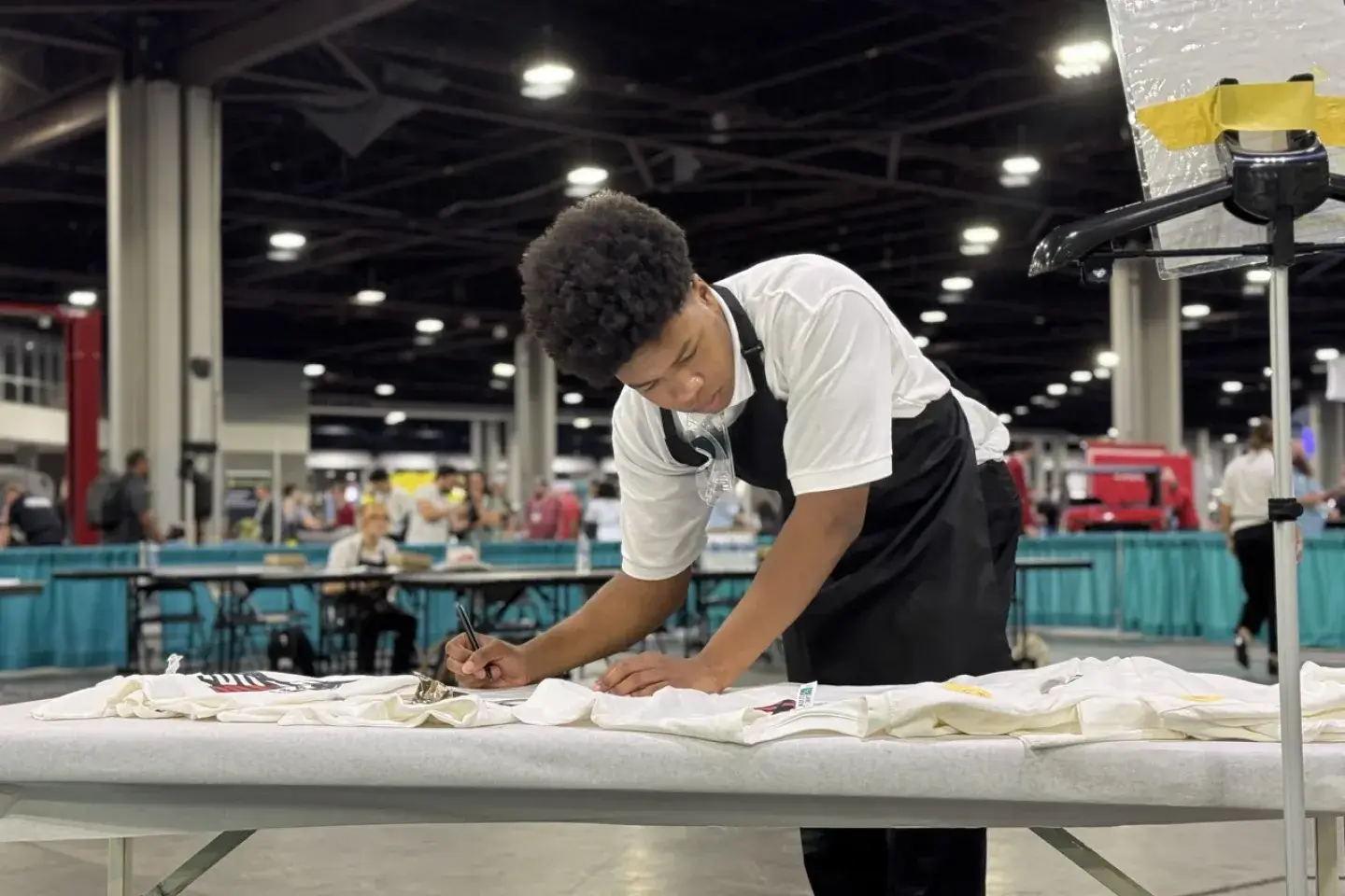 A male student wearing a smock working on designing shirts in a warehouse setting