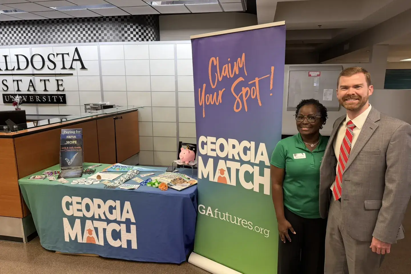 Two adults in business attire stand next to a exhibit booth for the GEORGIA MATCH program.
