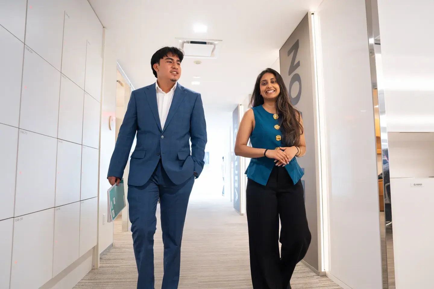 two young people are walking down an office hallway dressed in business clothes