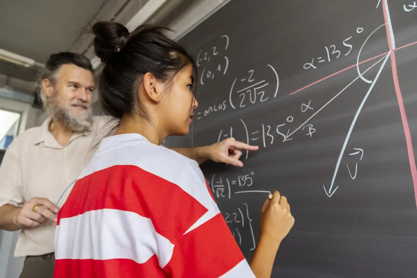 Mature caucasian male high school maths teacher explains blackboard exercise to asian girl teen student