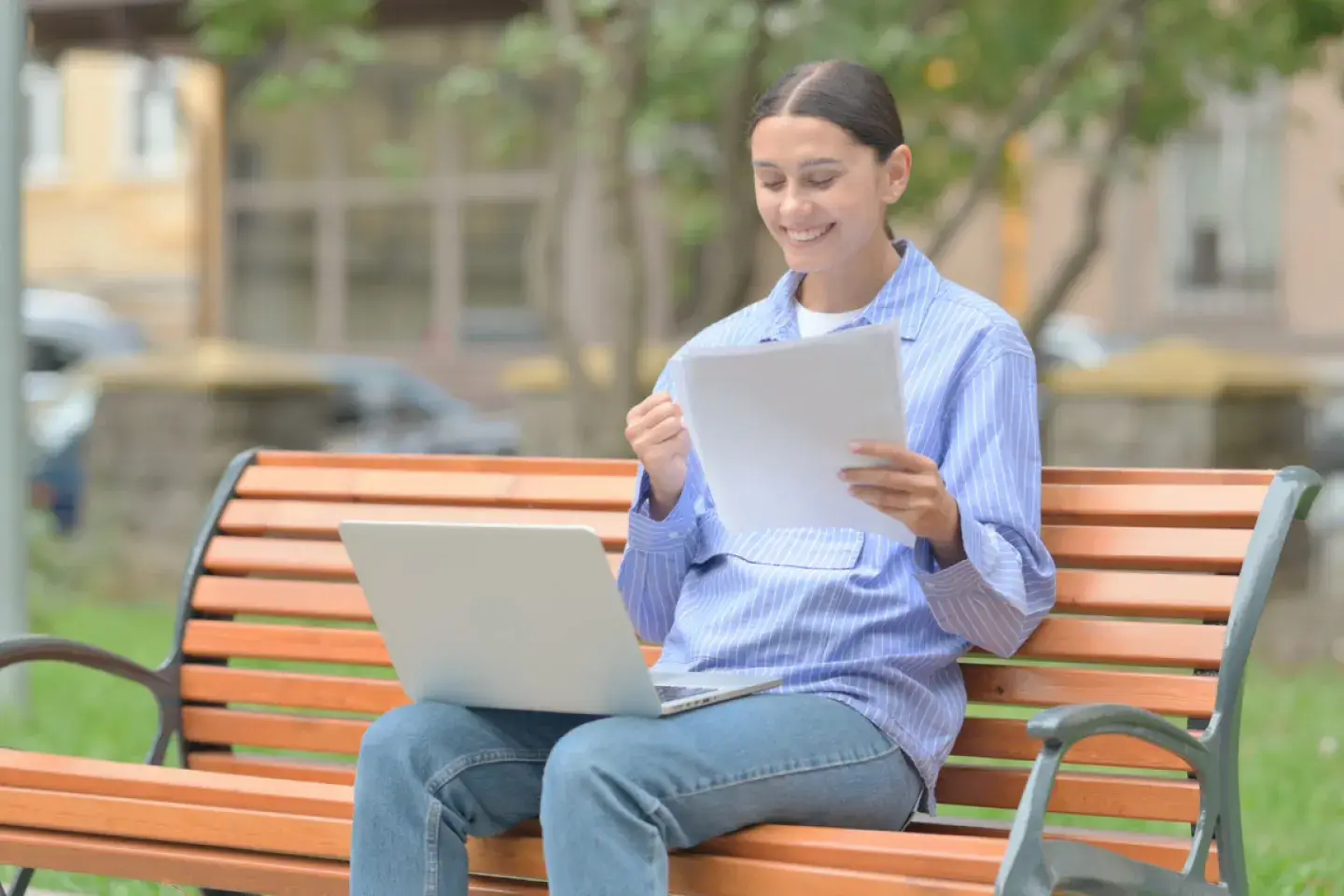 Hispanic Woman Celebrating while Working on Laptop and holding Documents