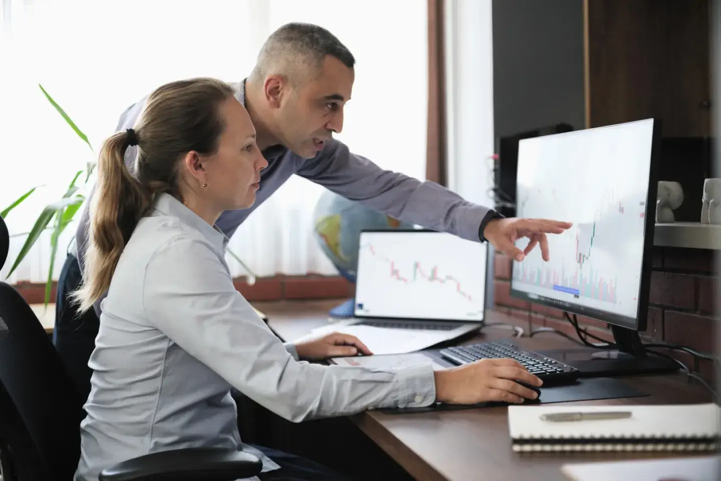 two businesspeople working in the office on stock market exchange data using desktop computer and digital tablet