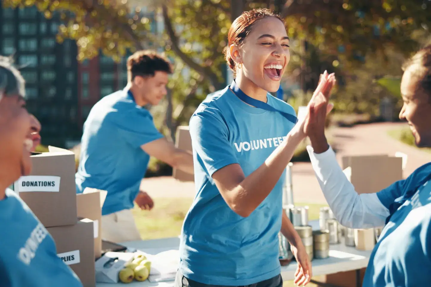 Two women in blue shirts that say "volunteer" high fiving while other volunteers organize boxes