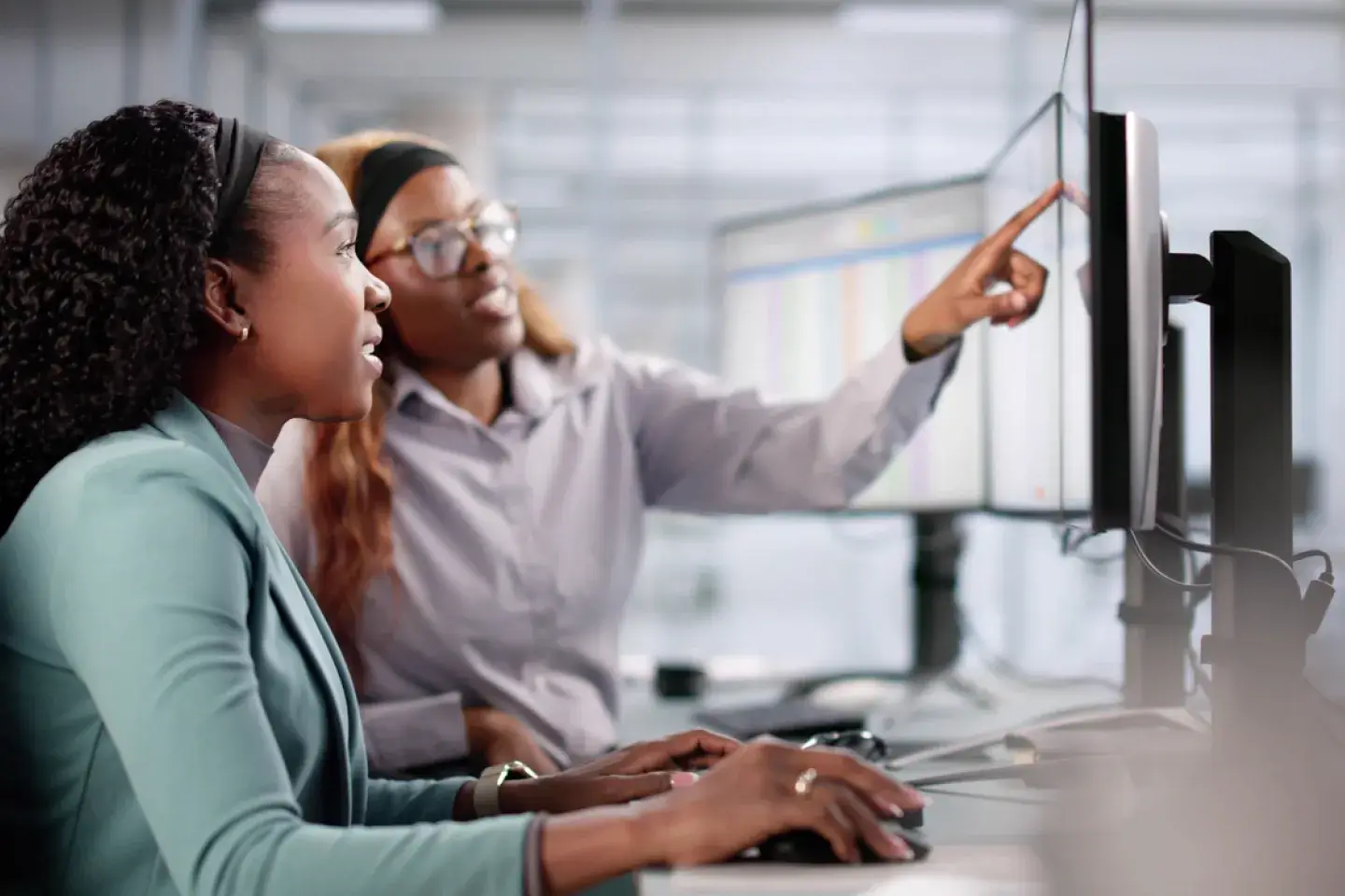 two young women working together at a computer dressed in business clothes