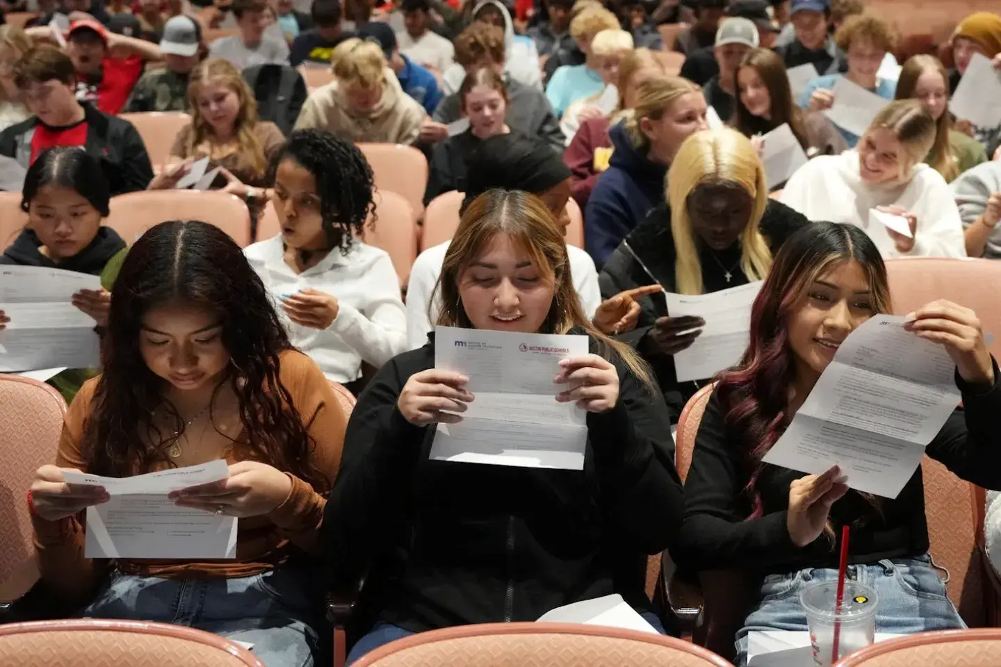 A group of students in an auditorium opening up college acceptance letters