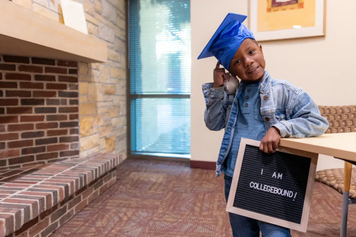 A young Black boy in a blue graduation cap holding a sign