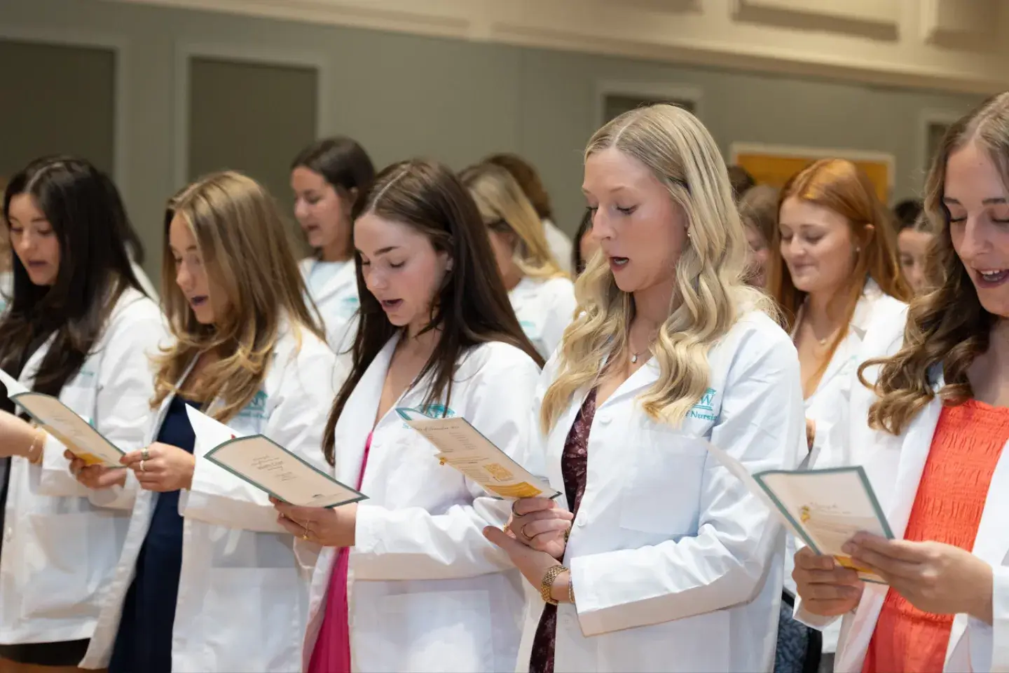 A group of young women in white coats reciting an oath