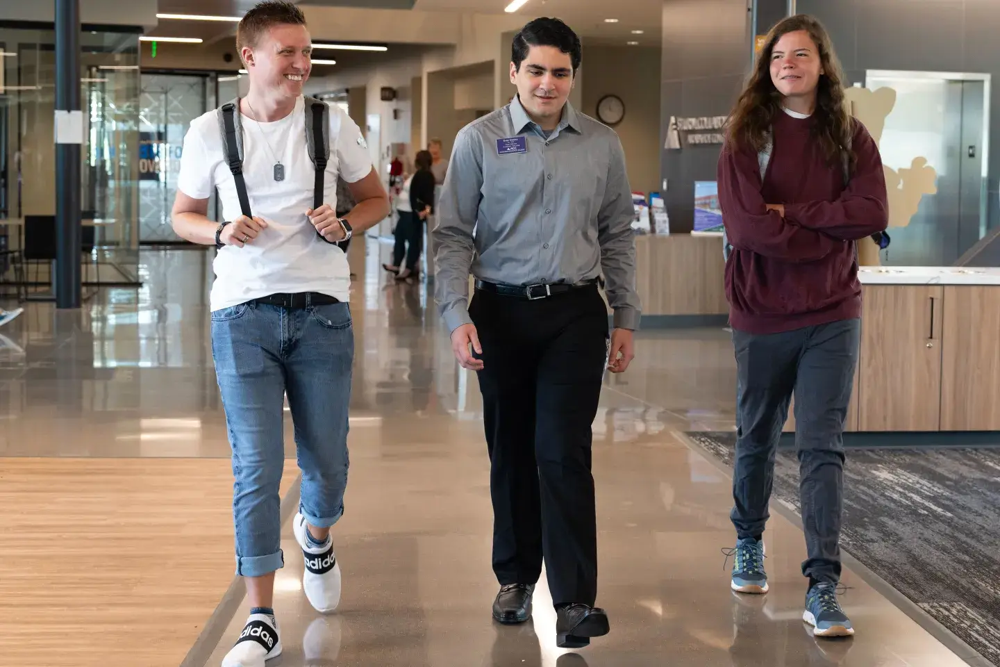 Three college students walk down a hall in a line.