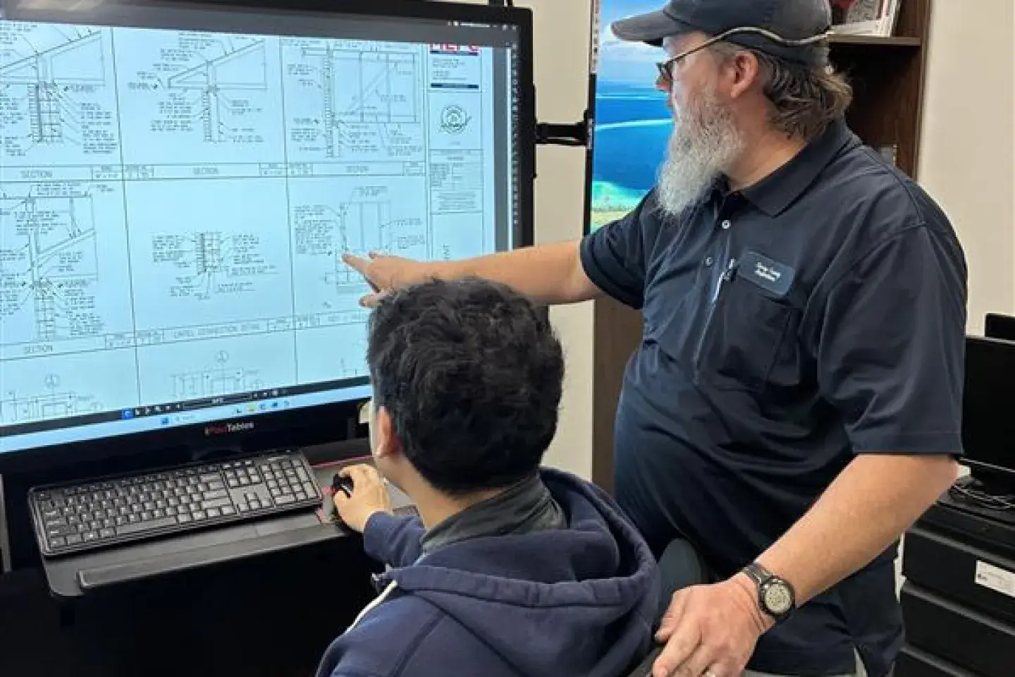 An older male helping a younger male look at data on a computer