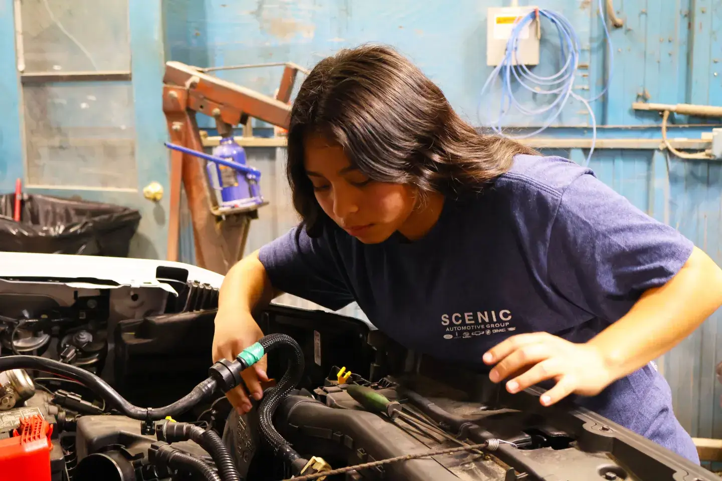 A young female works on a car with the hood up 