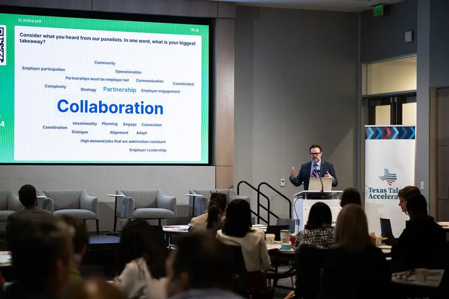 A man standing in front of a large powerpoint presentation in front of a large seated audience