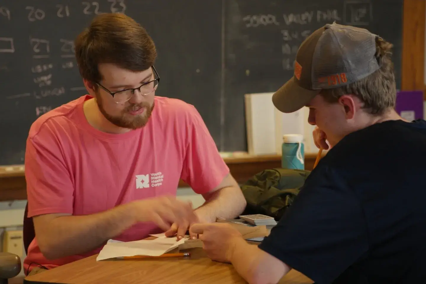 A male tutor in a pink t-shirt helps a student