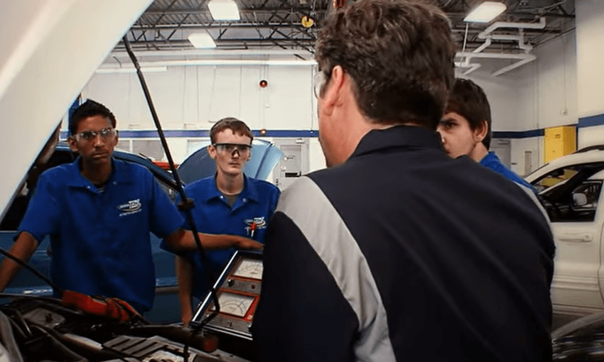 A few male students working on a car while an older male teaches them