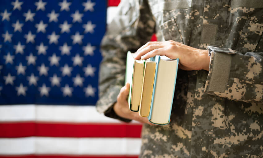Young Student Soldier In Uniform carrying books in front of an American flag