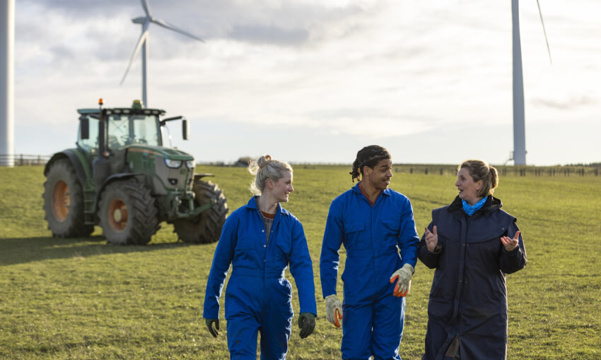 Young farmhands on the Job with wind turbines and a tractor behind them
