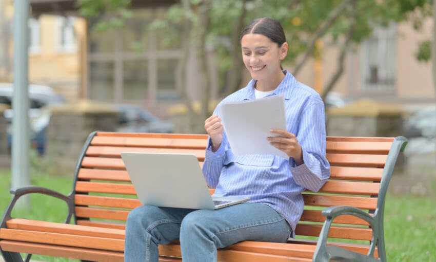 Hispanic Woman Celebrating while Working on Laptop and holding Documents