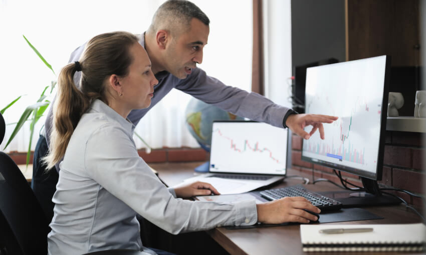 two businesspeople working in the office on stock market exchange data using desktop computer and digital tablet
