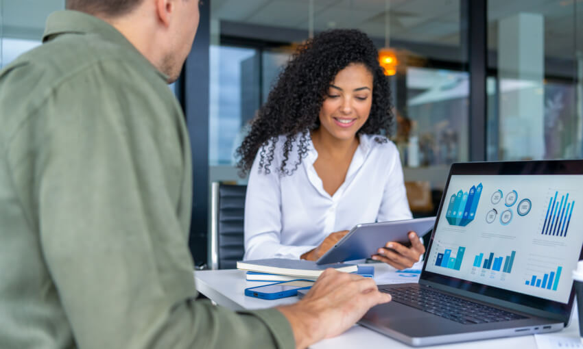 Business man and business woman in a meeting at the office. There is a laptop on the table showing finance charts and graphs