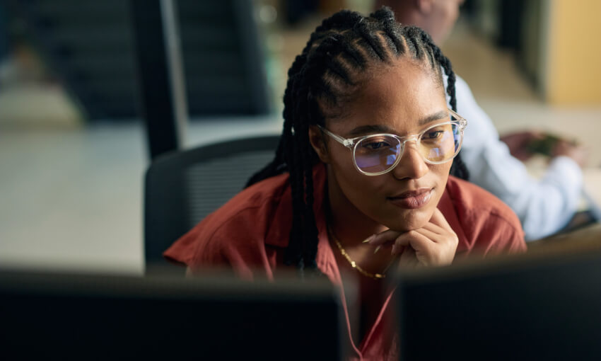 Young woman programmer focused on her work, coding on dual monitors in a modern office environment