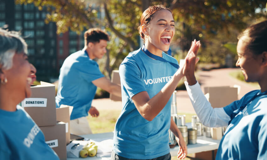 Two women in blue shirts that say "volunteer" high fiving while other volunteers organize boxes